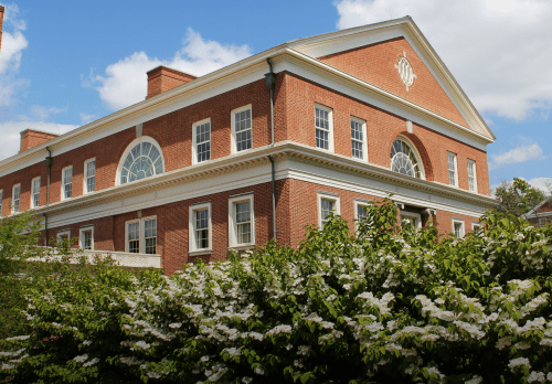 Exterior photo of Bavaro Hall it is a brick building with blue skies and flowers in the foreground