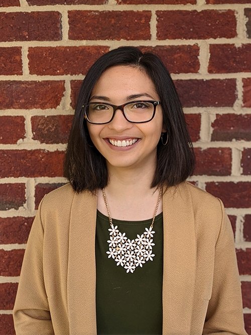 Alexis Prijoles standing in front of a brick wall and smiling at the camera