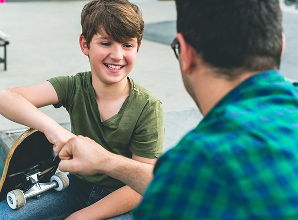 Boy with skateboard gives fist bump to adult