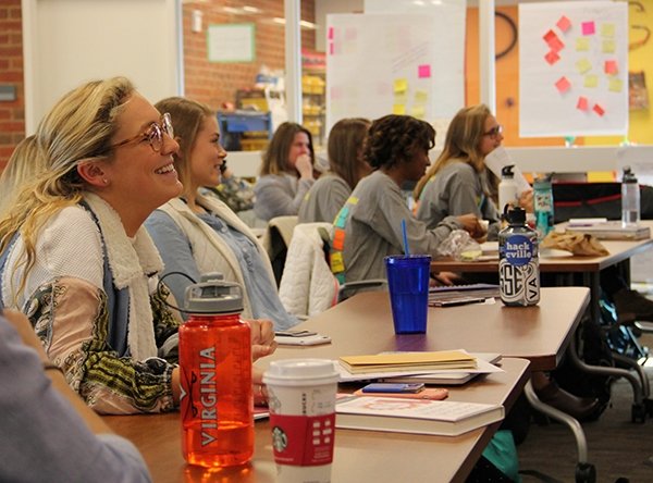 Students sit at a table smiling facing the direction.