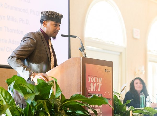 Man standing behind Youth-Nex podium speaking