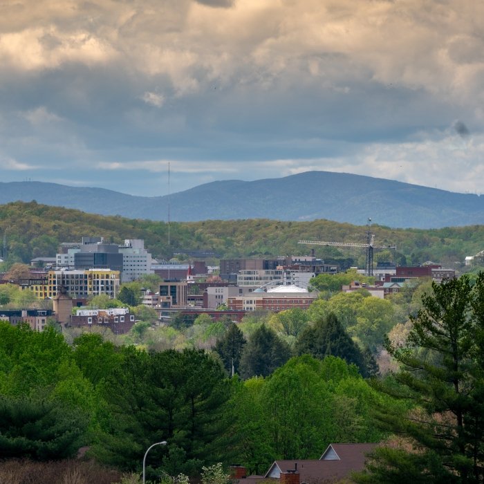 Wide-angle view of the city of Charlottesville with green trees in the foreground and the Blue Ridge Mountains in the background