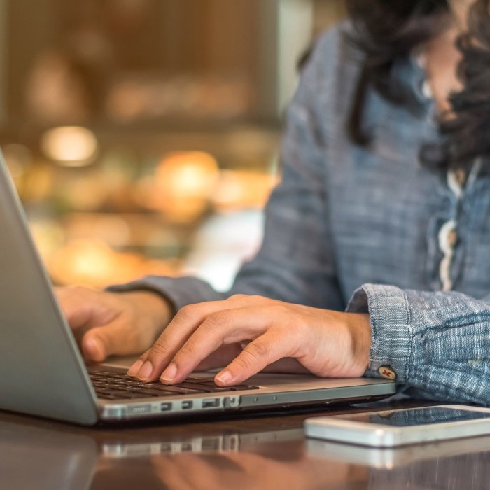 Close-up of a woman with dark hair and a blue shirt typing on a laptop