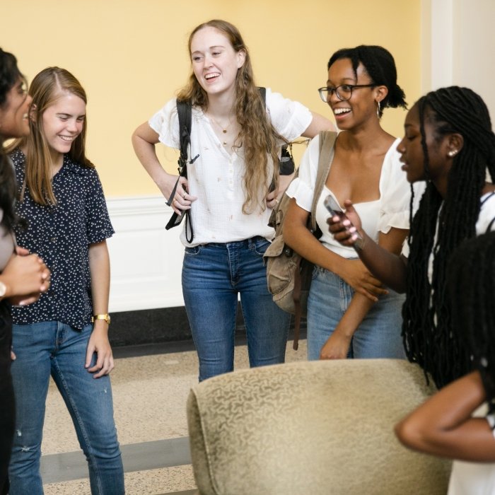 A small group of undergraduate students stand in a circle chatting and laughing