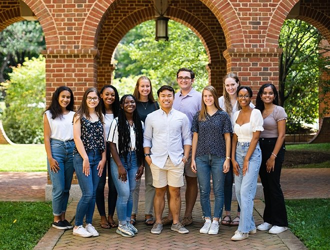 A group of student ambassadors stand outside in front of a brick archway
