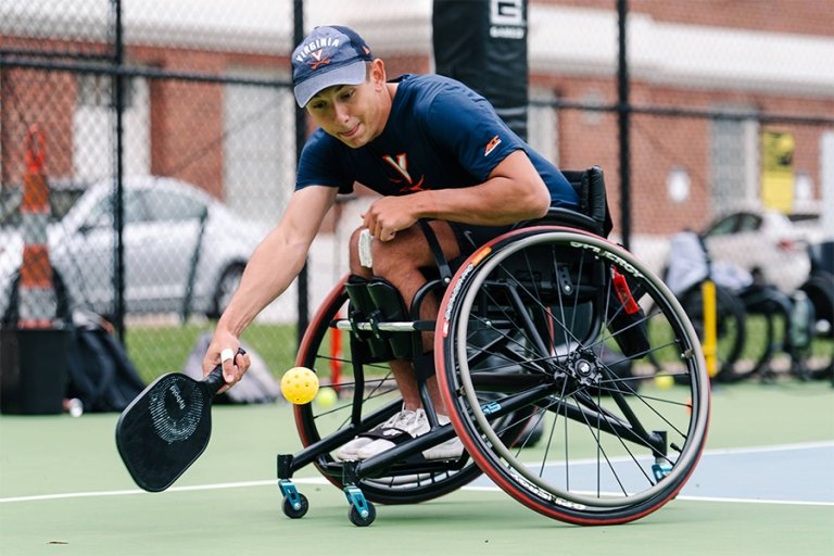 A student in a sport wheelchair leans down to hit the ball during a game of wheelchair pickleball