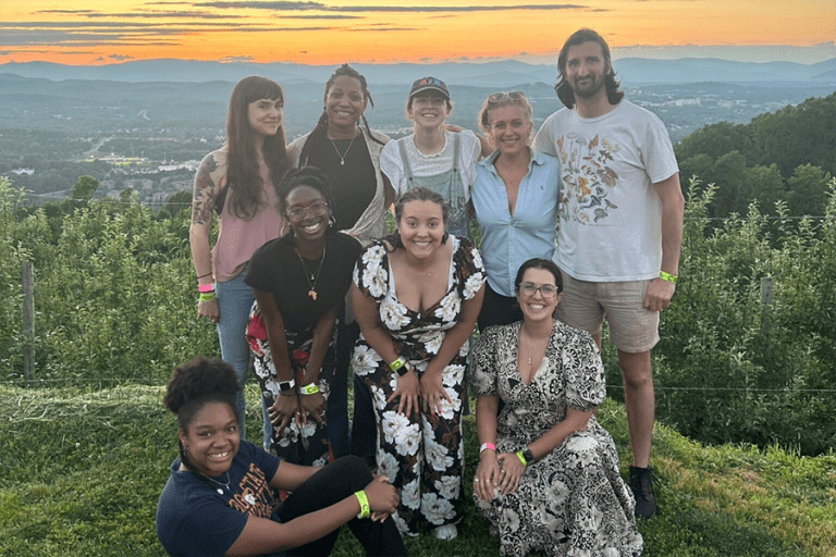 Students gather for a group photo outdoors in front of a sunset.