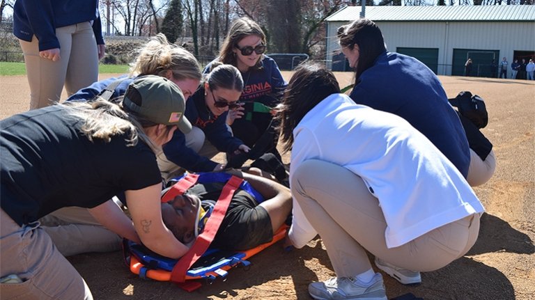 Several people gathered around a young man being strapped to a spineboard