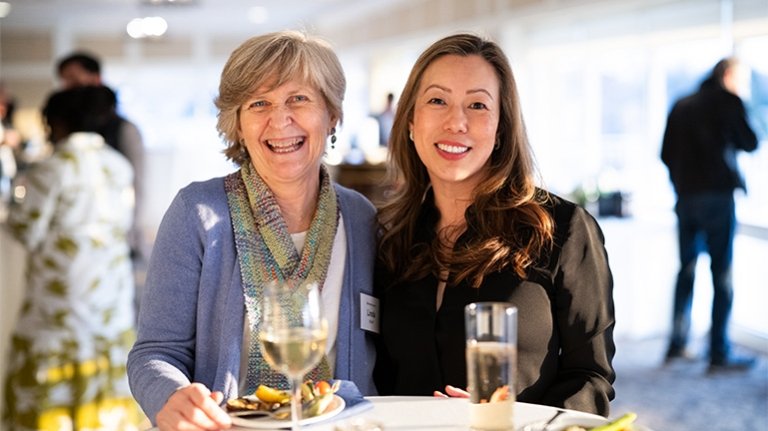Two individuals sitting at a table with wine and food.