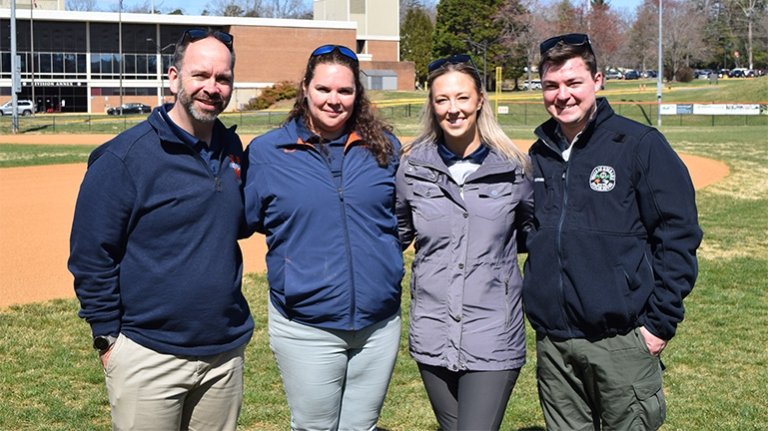 Four people standing outside on a baseball field