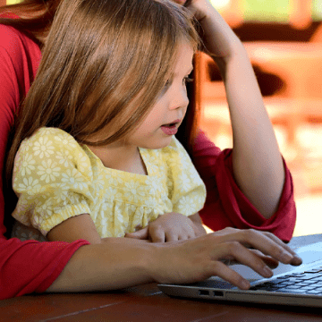A child sitting on their parents lap in front of a laptop