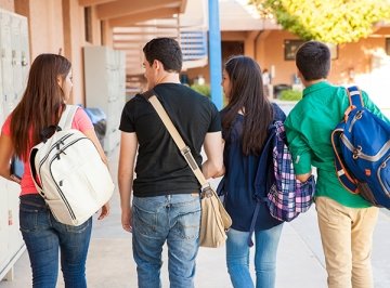 Students carrying backpacks walk away from camera at school