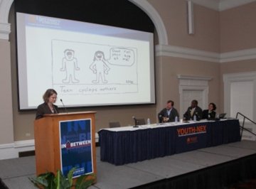 Speaker standing at podium with cartoon on screen behind.