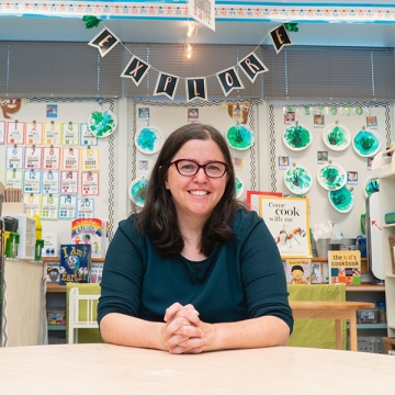 Daphna Bassok sits at table in kindergarten classroom and smiles at the camera