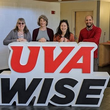 Four adults stand behind a large sign that reads UVA WISE