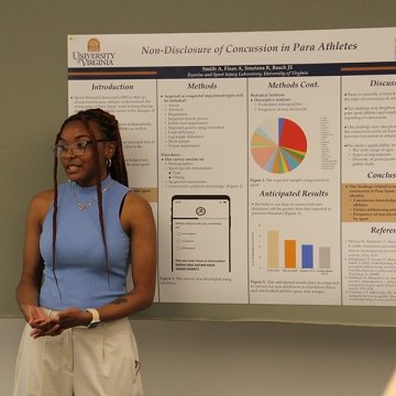 Kinesiology student Angela Smith stands in front of her research poster displayed on a large wall.